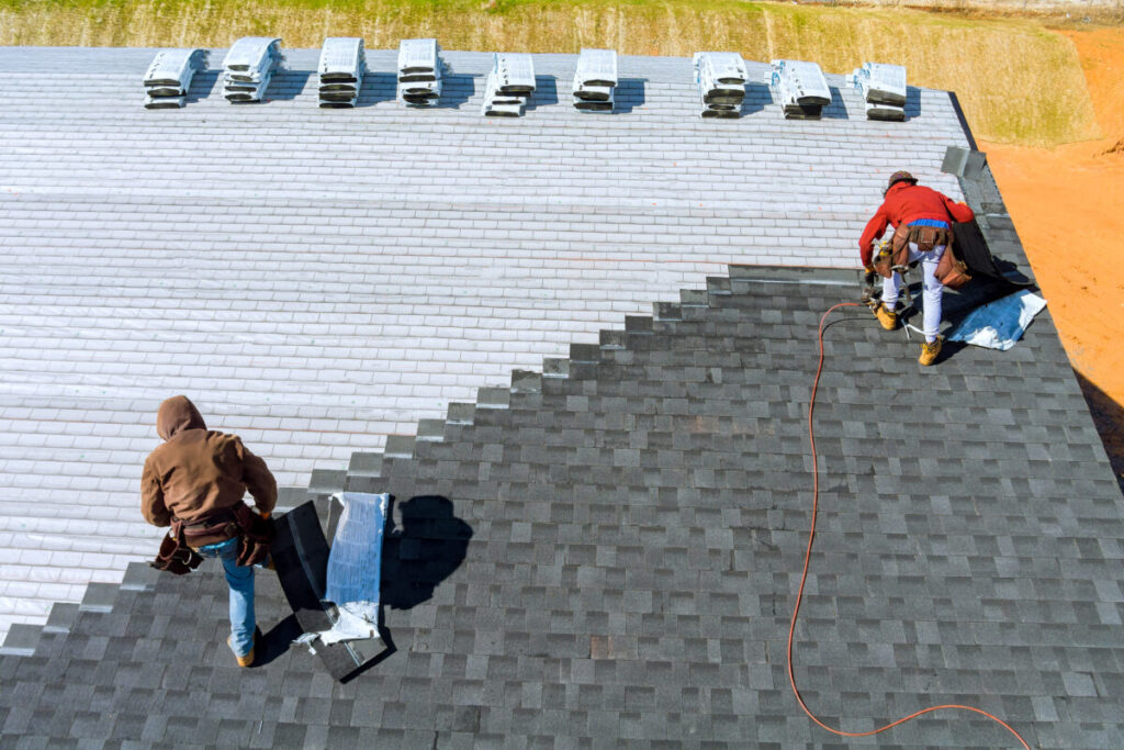 Roofing - Worker hands installing bitumen roof shingles with air hammer and nail